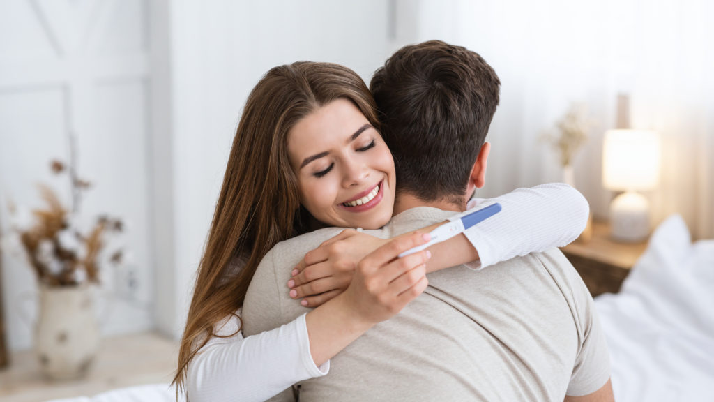 Mujer feliz abraza a su pareja con un test de embarazo